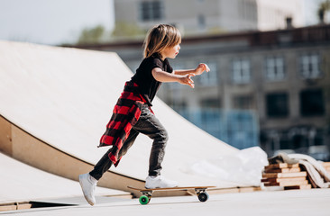 Funny boy dressed in the stylish casual clothes rides skateboard on a platform outside next to the...