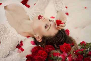Valentine's Day. Loving girl. The girl in a red dress lying on the floor in the petals of red roses.