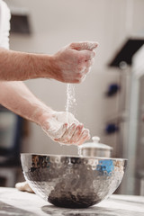 Baker adds flour to dough in an iron bowl on the table in the bakery