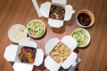 Top view of Chinese take away food with chop sticks on wooden table. Spicy asian food in white box - salad, souse, rice with egg, dry beef, crunchy chicken cooked in oil.