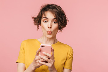 Shocked young beautiful woman posing isolated over pink wall background using mobile phone. - obrazy, fototapety, plakaty