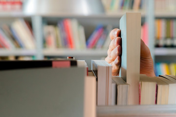 Young student picking a book from the shelf in the library. Preparing for exams, young man searching for or choosing a book in the public library in university