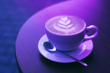 Freshly brewed cappuccino in a cup of white color on a wooden table in trendy neon light.