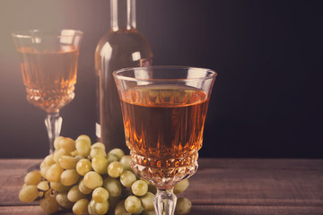 Two glasses of white wine, bottle and bunch of grapes standing on a wooden table