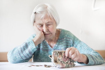 Concerned elderly 96 years old woman sitting at table at home and counting remaining coins from...