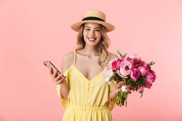 Beautiful excited happy amazing young blonde woman posing isolated over pink wall background holding flowers using mobile phone.