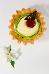 Creamy dessert with kiwi and cherry on top in a basket of shortcrust pastry с цветами жасмина on a white background