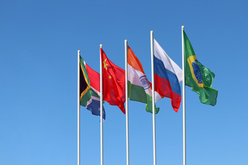 Waving flags of the BRICS countries against the clear blue sky. The summit of Brazil, Russia, India, China and South Africa