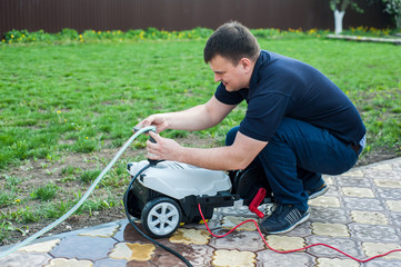 A man connects a hose to a portable car wash outside