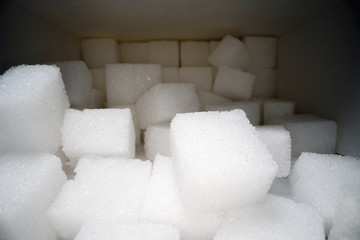 Macro shot of sugar cubes next to carton box on wooden table. Unhealthy food sweetener, sweet crystal cubes