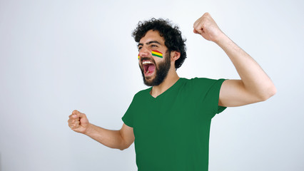 Sport fan screaming for the triumph of his team. Man with the flag of Bolivia makeup on his face and green t-shirt.