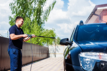 Man washing his car under high pressure water outdoors.