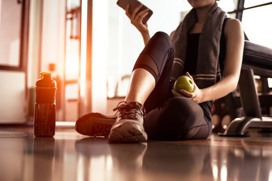 Close up of woman using smart phone and holding apple while workout in fitness gym. Sport and Technology concept. Lifestyles and Healthcare theme.