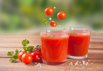 Tomato juice with parsley on the wooden table and flying cherry tomatoes