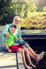 family, generation, technology, communication and people concept - grandfather and grandson with tablet pc computer sitting on river berth