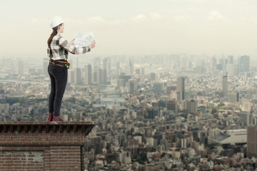 Female engineer holding construction plans standing on the roof top above a city