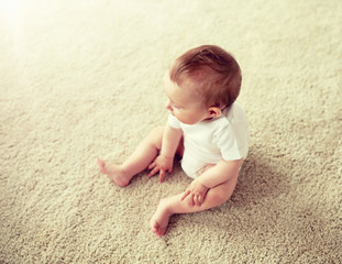 childhood, babyhood and people concept - happy little baby boy or girl sitting on floor at home