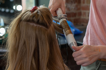 Fototapeta premium Stylist curling hair for young woman. Girl care about her hairstyle. To do curls