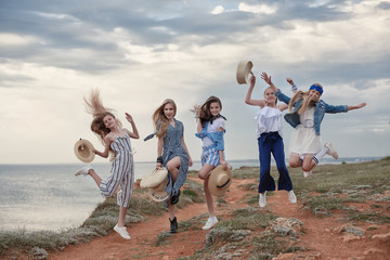 Five attractive and fun young girls having fun on the beach. Teenage sisters are resting together on the rocky shore of the blue ocean on a cloudy day against the blue sky and the coastline.