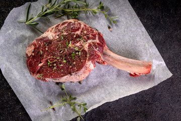 raw tomahawk steak on dark background with spices for grilling