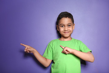Portrait of cute little boy pointing at something on color background