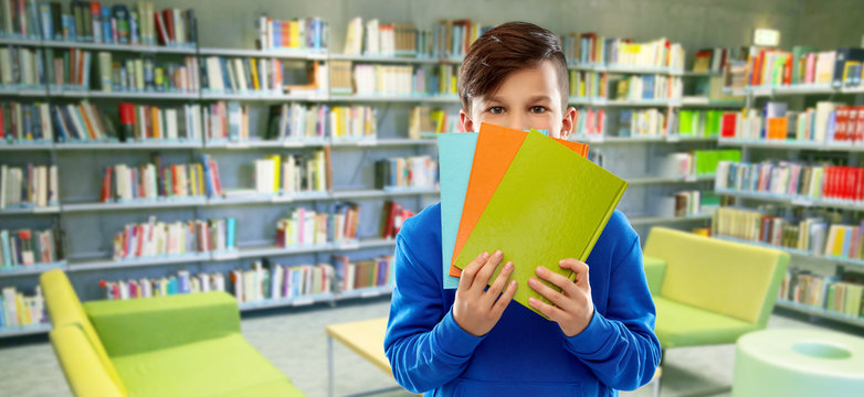 school, education and people concept - shy student boy hiding behind books over reading room of library background