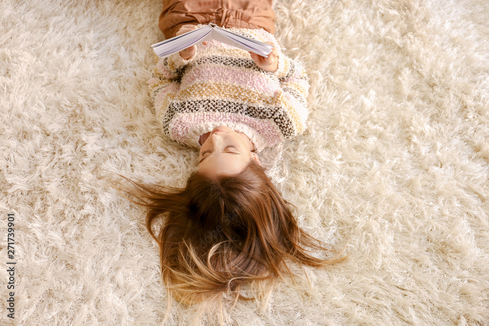 Poster Beautiful young woman reading book while lying on floor at home