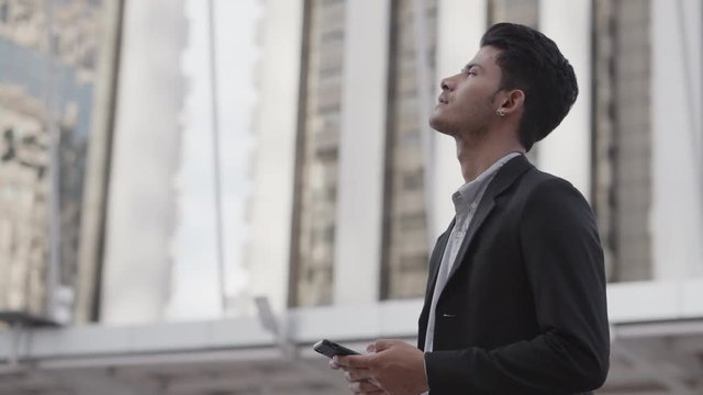 The image of a young Asian businessman standing outside the office. Young businessman wearing a suit Smiling and playing smart phone
