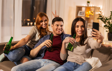 friendship and leisure concept - happy friends clinking drinks and taking selfie at home party in evening