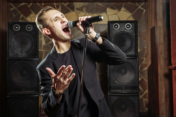 Portrait of handsome attractive singer singing hit with open mouth in microphone gesticulating with...