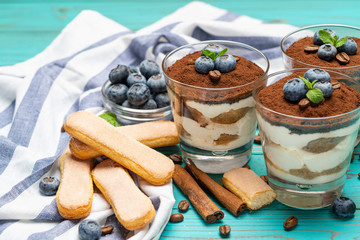 Classic tiramisu dessert in a glass with blueberries on blue wooden background
