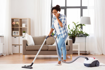 people, housework and housekeeping concept - happy african american woman with vacuum cleaner...