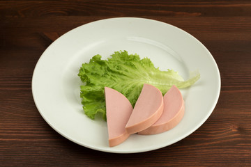 Slices of boiled sausage and lettuce with cherry tomatoes lie on a white plate.
