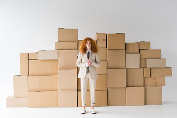 Curly redhead girl looking at camera while standing near boxes on white