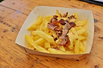 Close up of a paper plate with hot french fries with cheese and bacon.