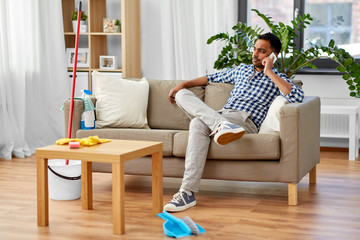 Fototapeta premium household and technology concept - indian man calling on smartphone after cleaning home