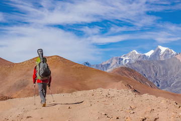 A man with a backpack and a guitar goes on the road to the mountains of Nepal. Rear view.
