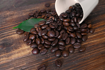 Brown arabica coffee beans with leaf and cup on a wooden board.