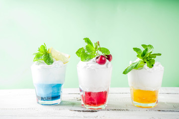 Summer cold drinks. Colorful Italian cream soda cocktails over white wooden background copy space