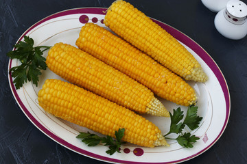Boiled corn is located on a plate on a dark background, top view