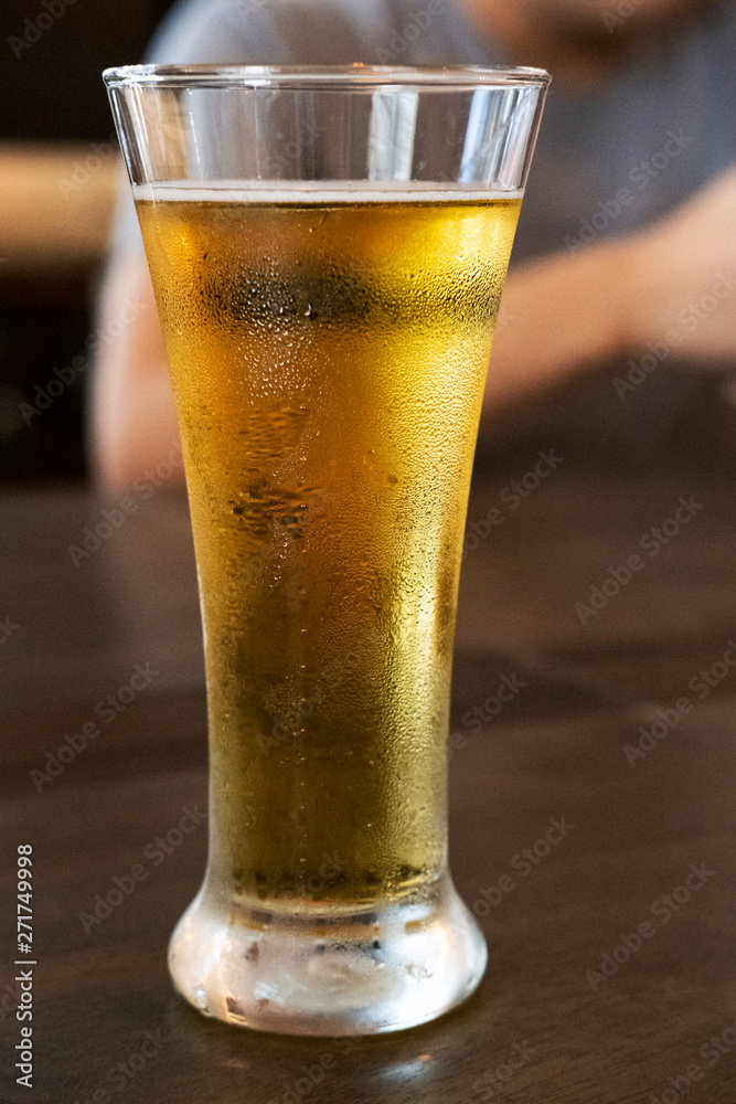 Wall mural cold beer in a tall glass on a wooden table