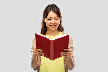 people, ethnicity and portrait concept - happy asian young woman reading book over grey background