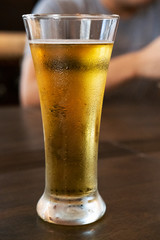 Cold beer in a tall glass on a wooden table