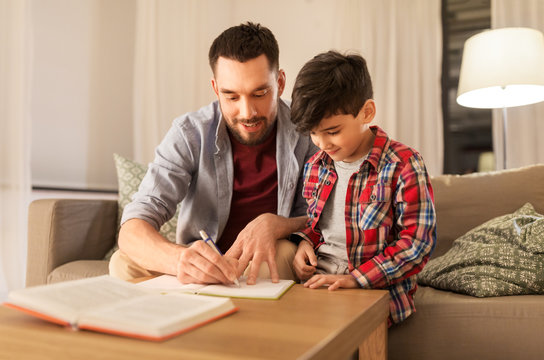 education, family and homework concept - happy father and son with book writing to notebook at home