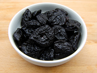 Dried plums in white dish on wooden background 