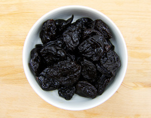 Dried plums in white dish on wooden background 