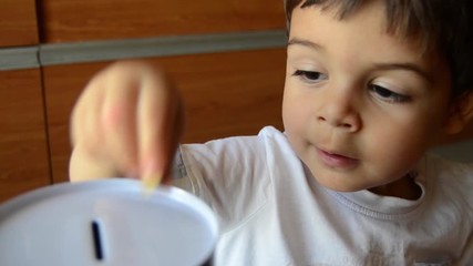 cute two years old saving money, putting coins in metal bank