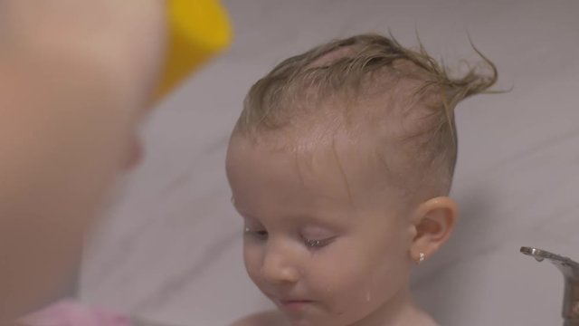 Attractive two years old girl takes a bath. Mom clean hair with a shampoo.