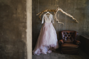 Modern bridal fashion. Lilac wedding dress hanging on a vintage branch inside the concrete loft interior.