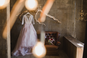 Modern bridal fashion. Lilac wedding dress hanging on a vintage branch inside the concrete loft...